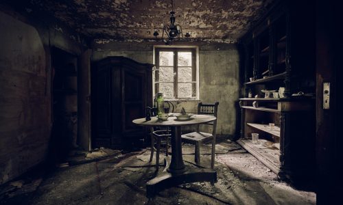 An abandoned room with a table in the middle and shelves against a wall near the window