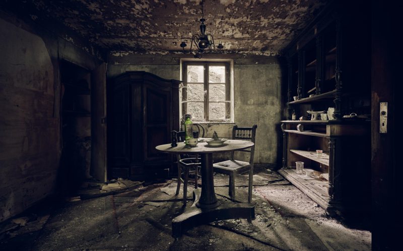 An abandoned room with a table in the middle and shelves against a wall near the window