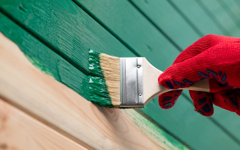 Close up of hand painting wooden wall with a brush. Painting outdoor building wall in green color