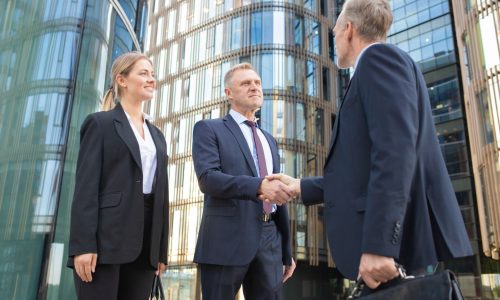 Confident business partners meeting in city, shaking hands near office building. Low angle shot. Cooperation and partnership concept