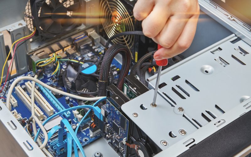Handyman is untightening a screw of the hard drive of the personal computer, close-up.