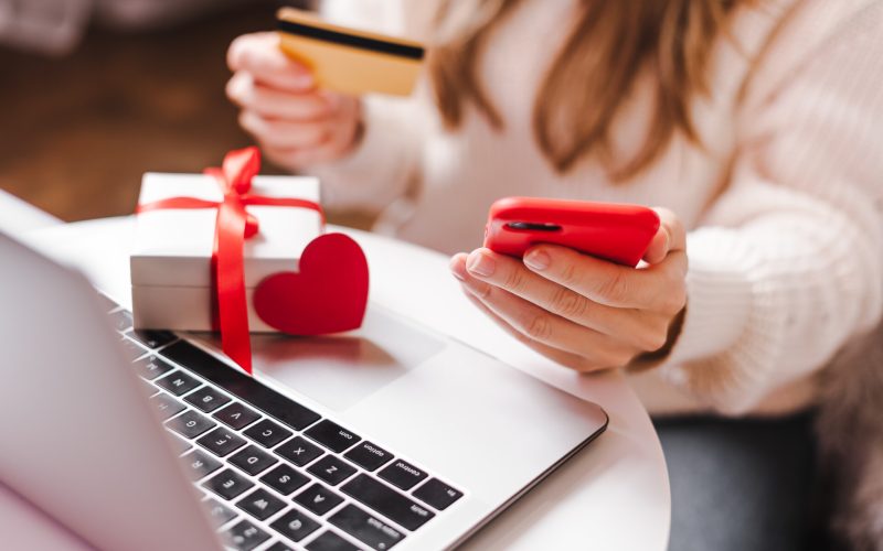 Close up of woman hands with mobile phone, credit card, gifts and laptop. Online shopping at Christmas, valentine day or birthday holidays. Freelance girl woking from home office