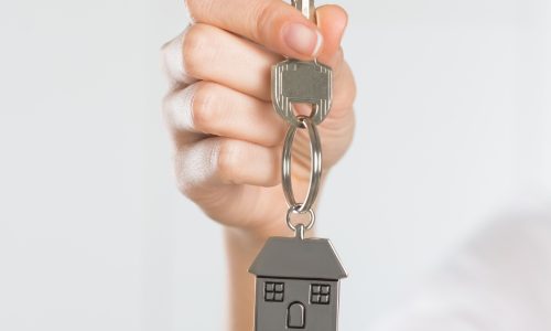Closeup shot of a woman holding key of her new house. Woman buying new home and showing key. Shallow depth of field with focus on house key.