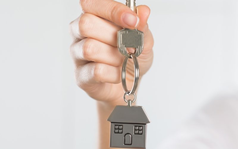Closeup shot of a woman holding key of her new house. Woman buying new home and showing key. Shallow depth of field with focus on house key.